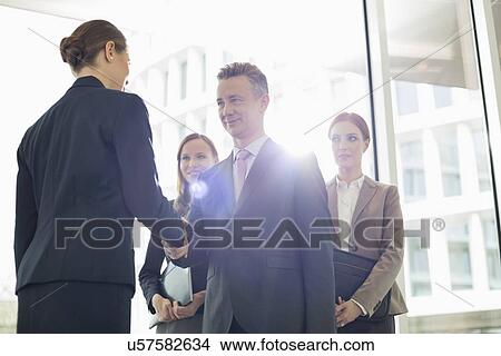 Confident business partners shaking hands in office View Large Photo Image Picture - Confident business partners shaking hands in office. Fotosearch