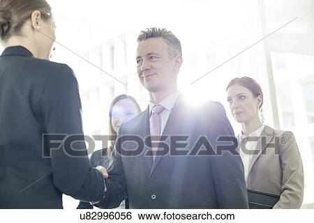 Confident business partners shaking hands in office View Large Photo Image Stock Photograph - Confident business partners shaking hands in office. Fotosearch