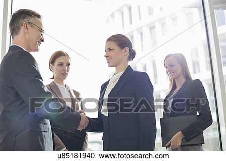Stock Image - Confident business people shaking hands in office. Fotosearch