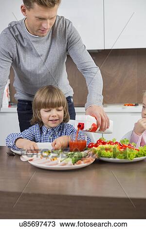 Father pouring juice for son at table in kitchen View Large Photo Image Stock Image - Father pouring juice for son at table in kitchen. Fotosearch