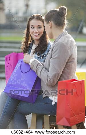 Female friends with shopping bags communicating while sitting on bench View Large Photo Image Picture - Female friends with shopping bags communicating while sitting on bench. Fotosearch