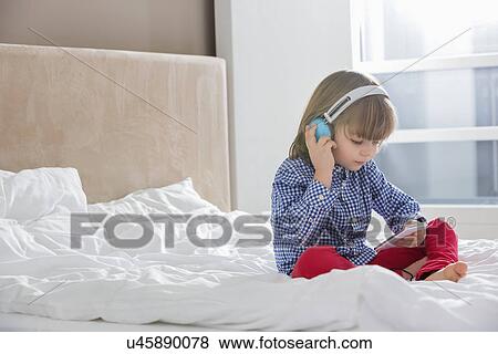 Full length of boy listening music on headphones in bedroom View Large Photo Image Stock Photo - Full length of boy listening music on headphones in bedroom. Fotosearch
