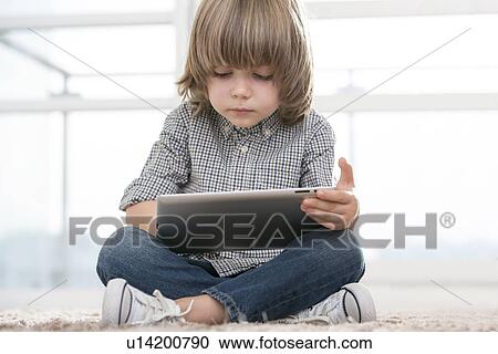 Stock Image - Full length of boy using digital tablet in living room. Fotosearch