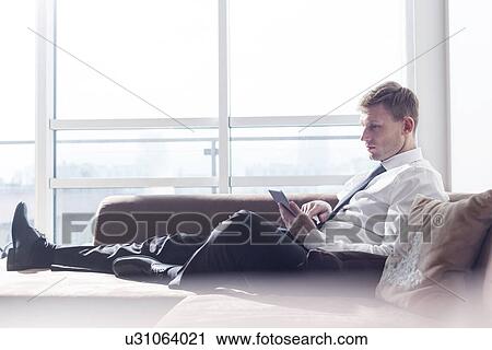 Full length of businessman using digital tablet on sofa at home View Large Photo Image Stock Image - Full length of businessman using digital tablet on sofa at home. Fotosearch