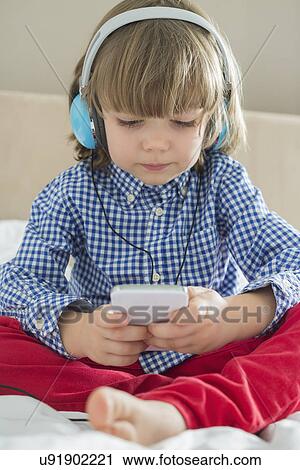 Full length of cute boy listening music on headphones in bedroom View Large Photo Image Stock Image - Full length of cute boy listening music on headphones in bedroom. Fotosearch