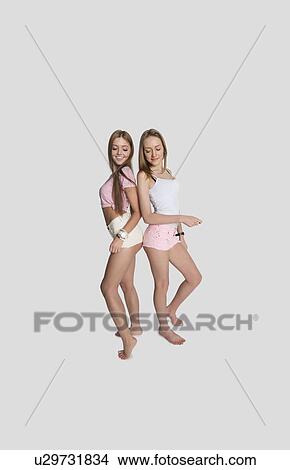 Picture - Full length of female friends wearing hot pants posing over gray background. Fotosearch