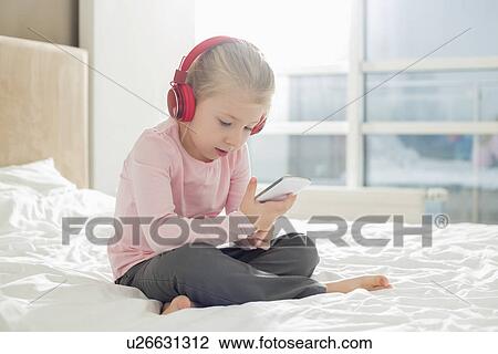 Stock Image - Full length of girl listening music on headphones in bedroom. Fotosearch