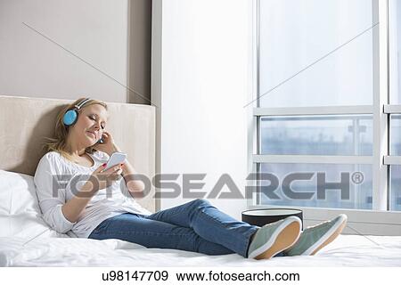 Full length of relaxed woman listening music in bedroom View Large Photo Image Stock Photo - Full length of relaxed woman listening music in bedroom. Fotosearch