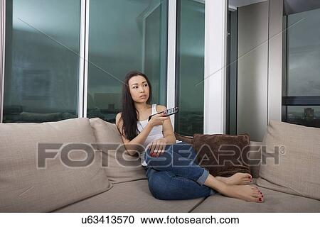 Full length of young woman watching TV in living room View Large Photo Image Stock Image - Full length of young woman watching TV in living room. Fotosearch