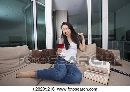 Stock Photograph - Full length portrait of happy young woman having red wine in living room. Fotosearch