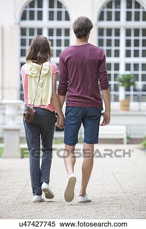 Full-length rear view of young couple walking against building View Large Photo Image Stock Photography - Full-length rear view of young couple walking against building. Fotosearch