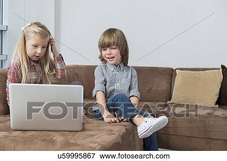 Stock Photo - Happy boy with sister using laptop on sofa. Fotosearch