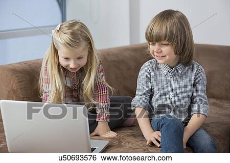 Stock Photograph - Happy boy with sister using laptop on sofa. Fotosearch