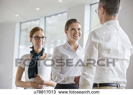 Stock Image - Happy business people shaking hands in office. Fotosearch
