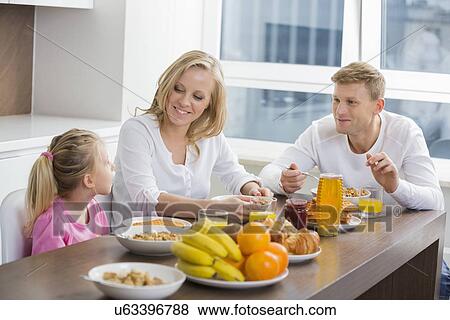 Stock Photo - Happy family of three having breakfast at table. Fotosearch