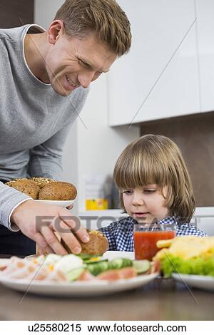Happy father serving meal to son at table in kitchen View Large Photo Image Stock Photography - Happy father serving meal to son at table in kitchen. Fotosearch