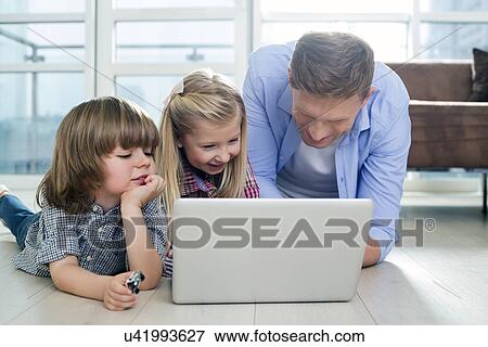 Happy father with children using laptop on floor in living room View Large Photo Image Stock Photo - Happy father with children using laptop on floor in living room. Fotosearch