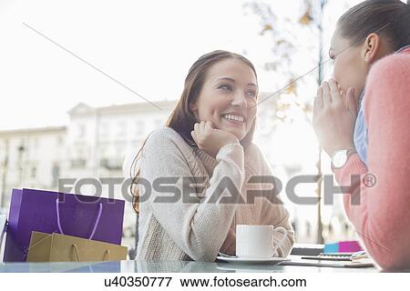 Stock Photo - Happy female friends gossiping at outdoor cafe. Fotosearch