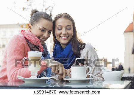 Happy female friends using cell phone at sidewalk cafe View Large Photo Image Stock Image - Happy female friends using cell phone at sidewalk cafe. Fotosearch
