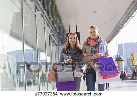Happy female friends with shopping bags walking on sidewalk View Large Photo Image Picture - Happy female friends with shopping bags walking on sidewalk. Fotosearch