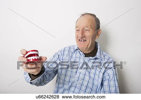 Happy senior man holding dentures against gray background View Large Photo Image Stock Photo - Happy senior man holding dentures against gray background. Fotosearch