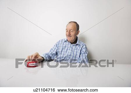 Stock Photograph - Happy senior man with dentures at table. Fotosearch