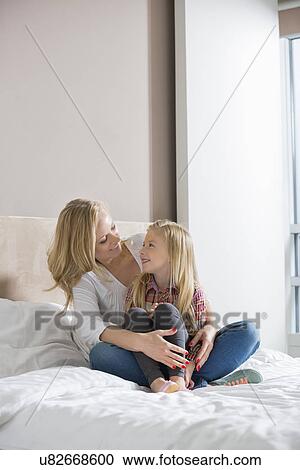 Stock Image - Happy woman and daughter looking at each other in bedroom. Fotosearch