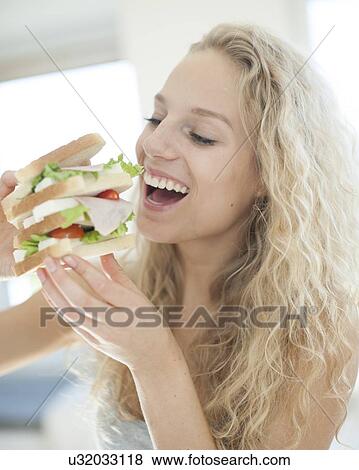 Happy woman eating large sandwich in house View Large Photo Image Stock Photo - Happy woman eating large sandwich in house. Fotosearch