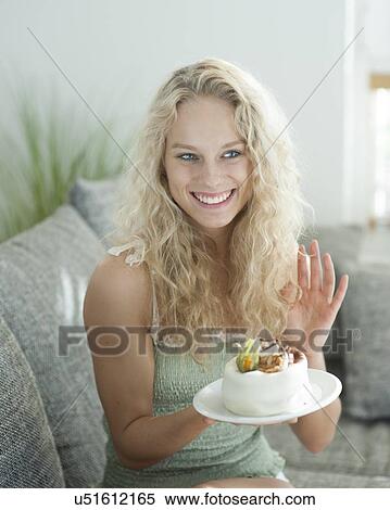 Stock Photography - Happy woman gesturing while holding cake in house. Fotosearch