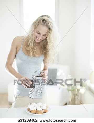 Happy woman grating chocolate on cupcakes at counter View Large Photo Image Stock Image - Happy woman grating chocolate on cupcakes at counter. Fotosearch