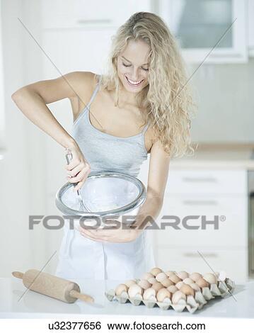 Stock Photograph - Happy woman mixing cookie batter in kitchen at counter. Fotosearch