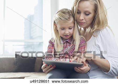 Happy woman with daughter using digital tablet in living room View Large Photo Image Stock Image - Happy woman with daughter using digital tablet in living room. Fotosearch