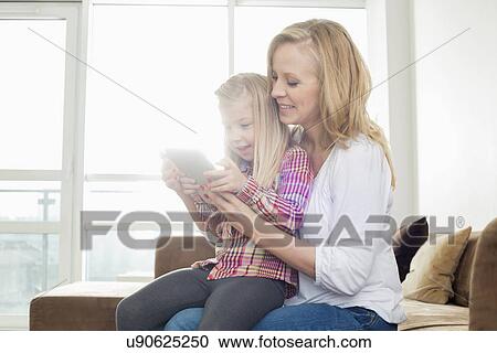Happy woman with daughter using digital tablet in living room View Large Photo Image Stock Image - Happy woman with daughter using digital tablet in living room. Fotosearch