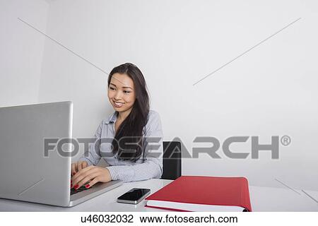 Happy young businesswoman using laptop at office desk View Large Photo Image Stock Image - Happy young businesswoman using laptop at office desk. Fotosearch