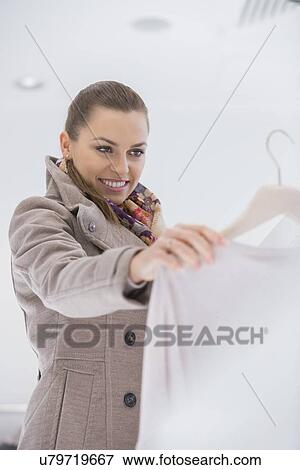 Happy young woman choosing sweater in store View Large Photo Image Stock Photo - Happy young woman choosing sweater in store. Fotosearch
