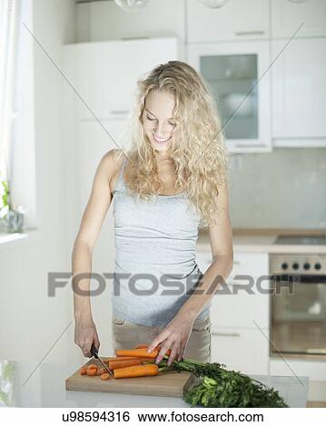 Happy young woman chopping carrots on board in kitchen View Large Photo Image Stock Photograph - Happy young woman chopping carrots on board in kitchen. Fotosearch