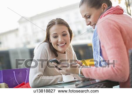 Happy young woman showing text message to friend at sidewalk cafe View Large Photo Image Stock Photo - Happy young woman showing text message to friend at sidewalk cafe. Fotosearch