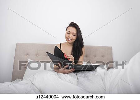 Picture - Happy young woman with spiral notepad in bedroom. Fotosearch