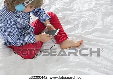 High angle view of boy listening to music through smart phone in bedroom View Large Photo Image Stock Image - High angle view of boy listening to music through smart phone in bedroom. Fotosearch