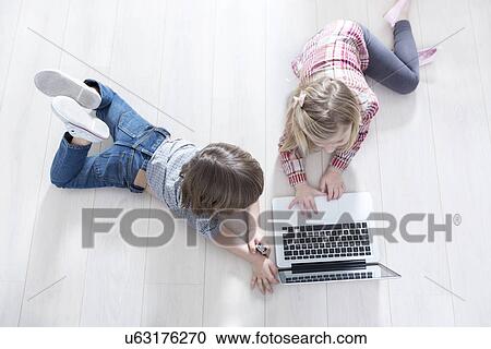 Stock Image - High angle view of brother and sister using laptop on floor at home. Fotosearch