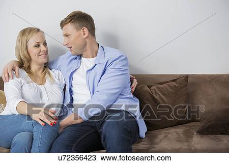 Loving mid adult couple sitting on sofa at home View Large Photo Image Stock Image - Loving mid adult couple sitting on sofa at home. Fotosearch