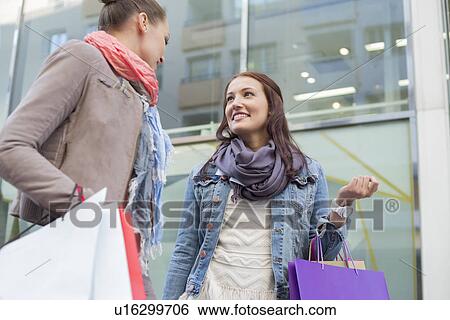 Low angle view of female friends with shopping bags looking at each other against store View Large Photo Image Stock Photograph - Low angle view of female friends with shopping bags looking at each other against store. Fotosearch