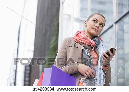 Low angle view of young woman listening to music while shopping View Large Photo Image Picture - Low angle view of young woman listening to music while shopping. Fotosearch