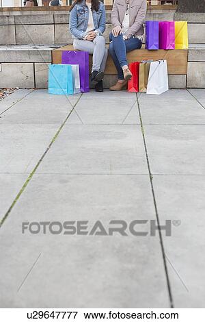 Low section of female friends with shopping bags sitting on steps with sidewalk on foreground View Large Photo Image Stock Photo - Low section of female friends with shopping bags sitting on steps with sidewalk on foreground. Fotosearch