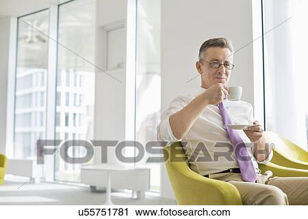 Stock Image - Mature businessman having coffee at office lobby. Fotosearch