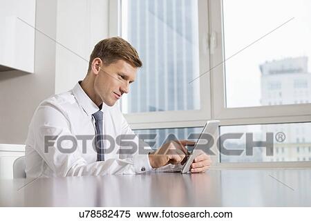 Mid adult businessman using digital tablet at kitchen table View Large Photo Image Stock Photography - Mid adult businessman using digital tablet at kitchen table. Fotosearch