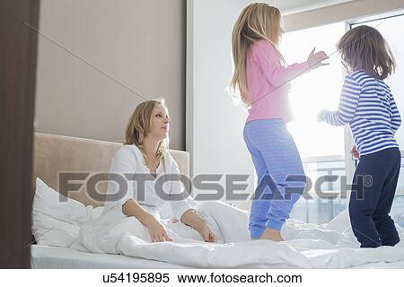 Stock Photography - Mid adult parents looking at playful children in bedroom. Fotosearch