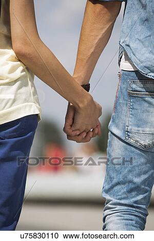 Stock Image - Mid section of couple holding hands outdoors. Fotosearch