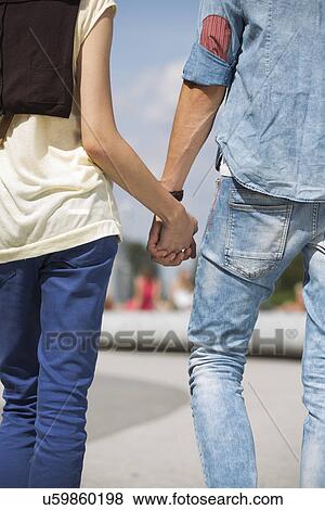 Mid section rear view of couple holding hands outdoors View Large Photo Image Stock Photo - Mid section rear view of couple holding hands outdoors. Fotosearch