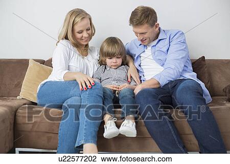 Stock Image - Parents sitting with sad son on sofa at home. Fotosearch